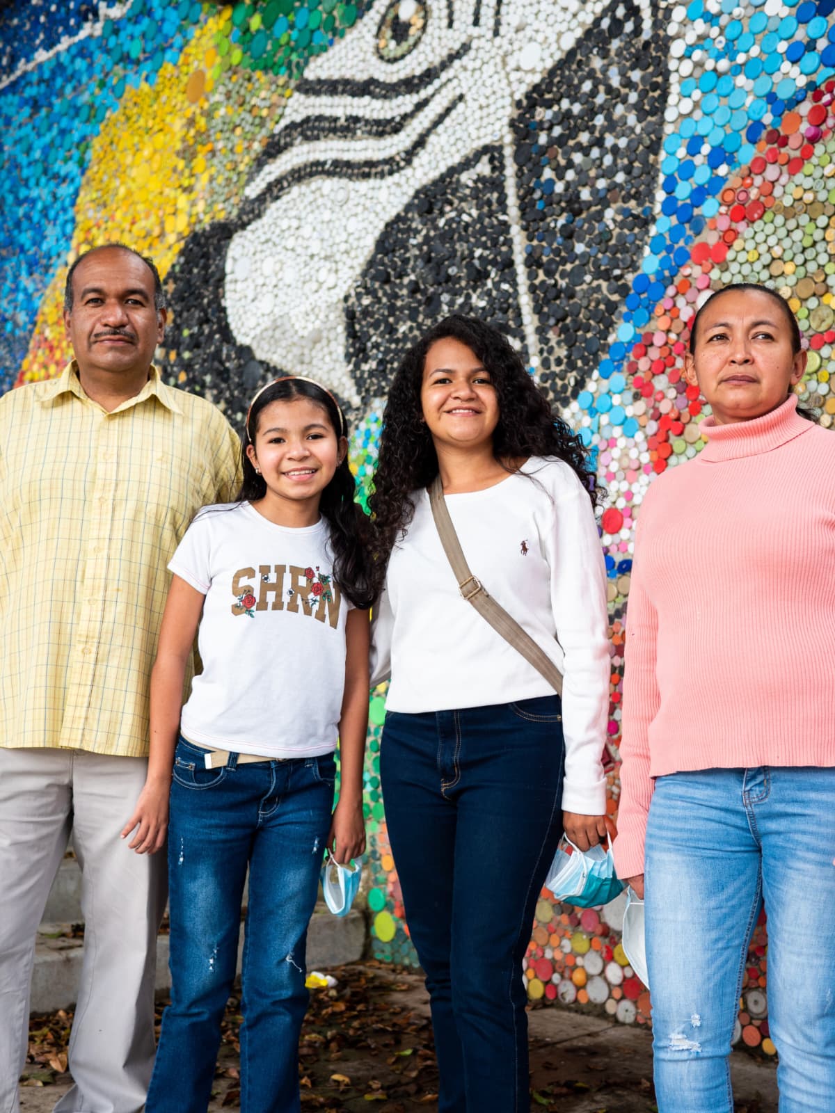A family standing together in front of a bright community mural